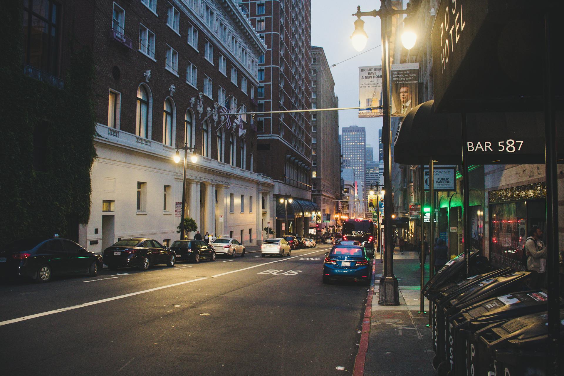 Lively urban street at dusk with cars and illuminated buildings, showcasing city life.