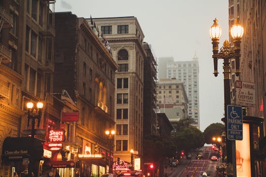 傍晚时分，雾中可见繁忙的城市街道，两旁建筑灯火通明，街灯闪烁