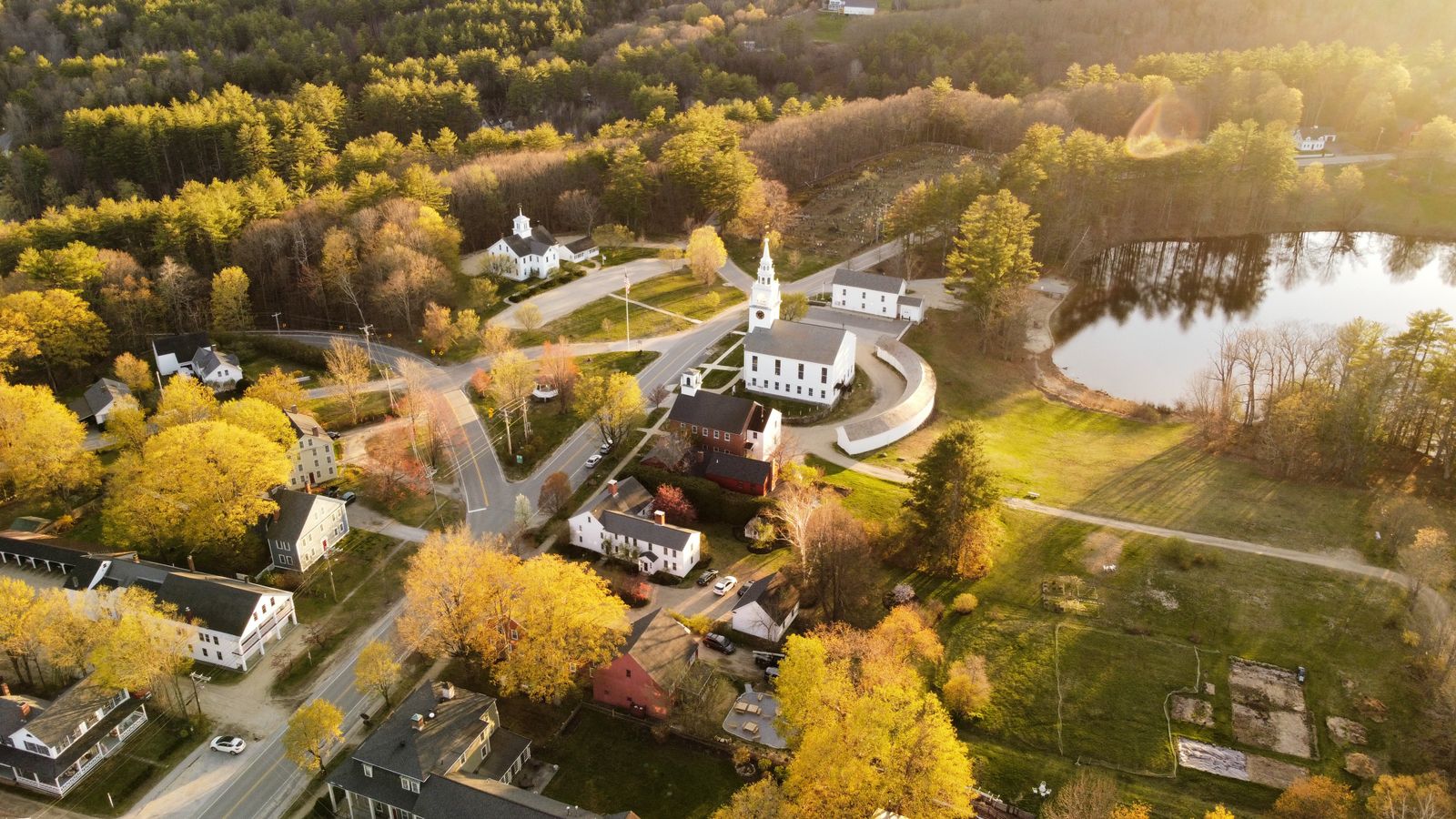 Aerial view of Hancock, NH showcasing fall foliage, a church, and a tranquil lake.