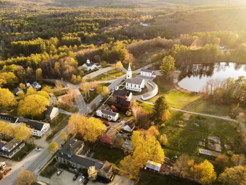Free Aerial view of Hancock, NH showcasing fall foliage, a church, and a tranquil lake. Stock Photo
