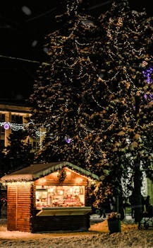 A cozy Christmas market stall illuminated with lights, surrounded by snow-covered trees at night.