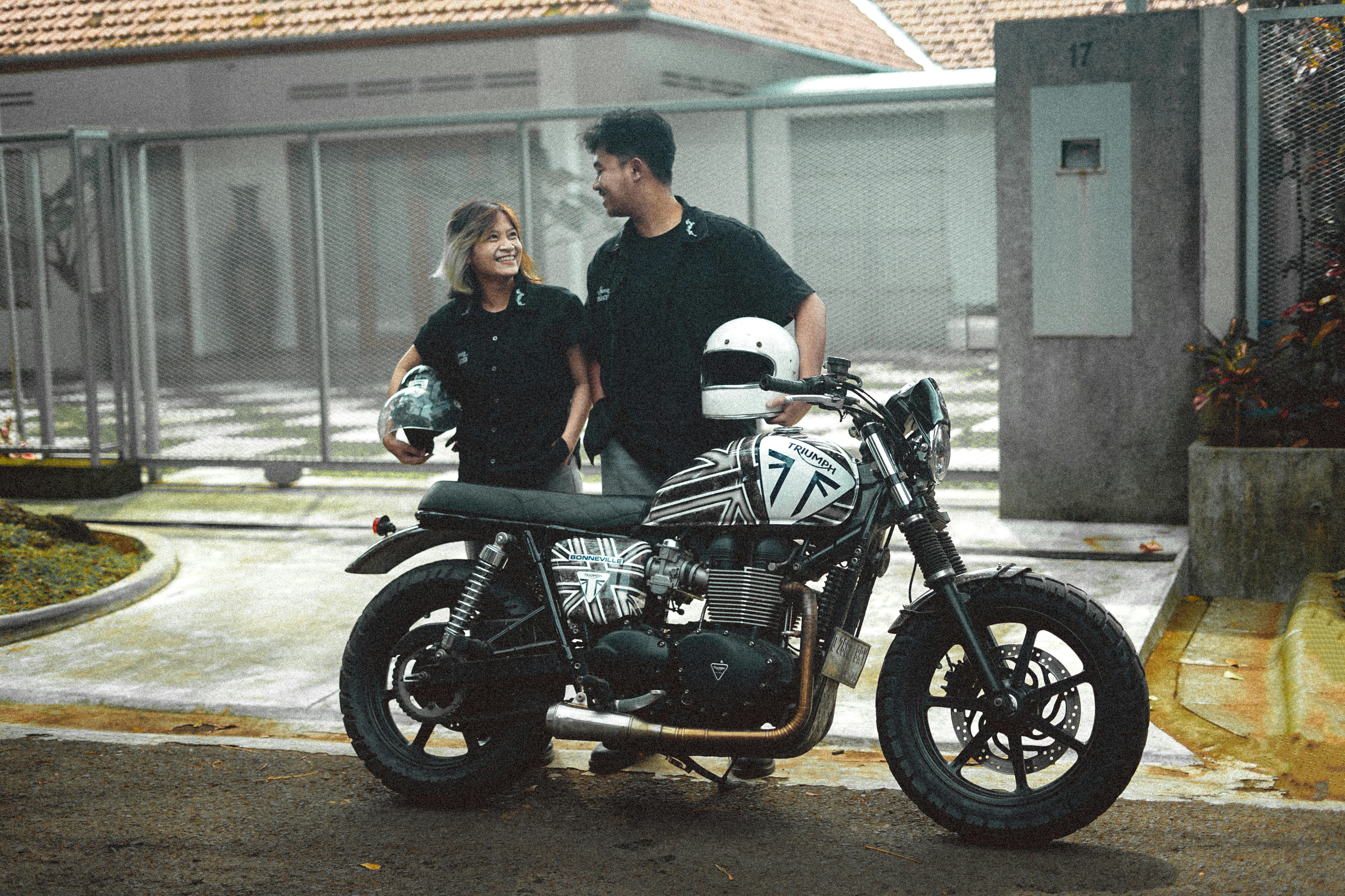 A couple in black shirts standing beside a Triumph motorcycle, enjoying the outdoors.