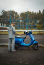 Man in White Jacket Standing Beside Blue Motor Scooter
