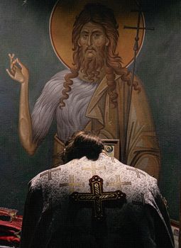 Orthodox priest in prayer before religious icon inside a church, symbolizing faith and devotion.