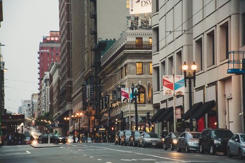 Free Bustling city street with lined cars and historic architecture, capturing vibrant urban life. Stock Photo