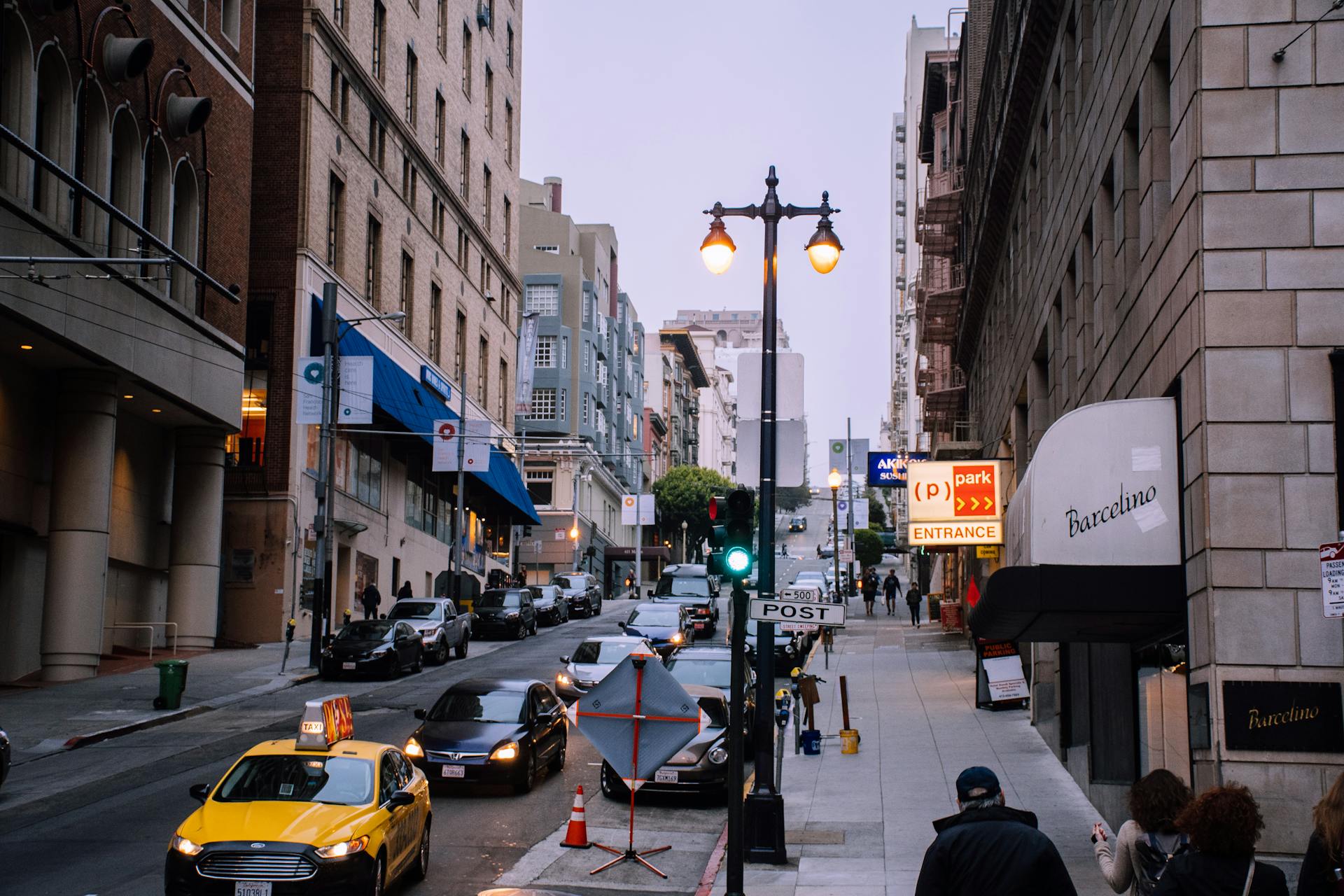 A busy urban street with cars, pedestrians, and storefronts at dusk.