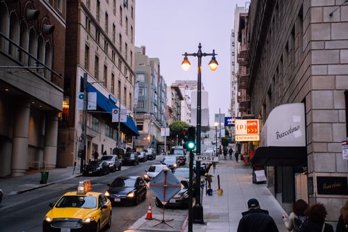 Free A busy urban street with cars, pedestrians, and storefronts at dusk. Stock Photo