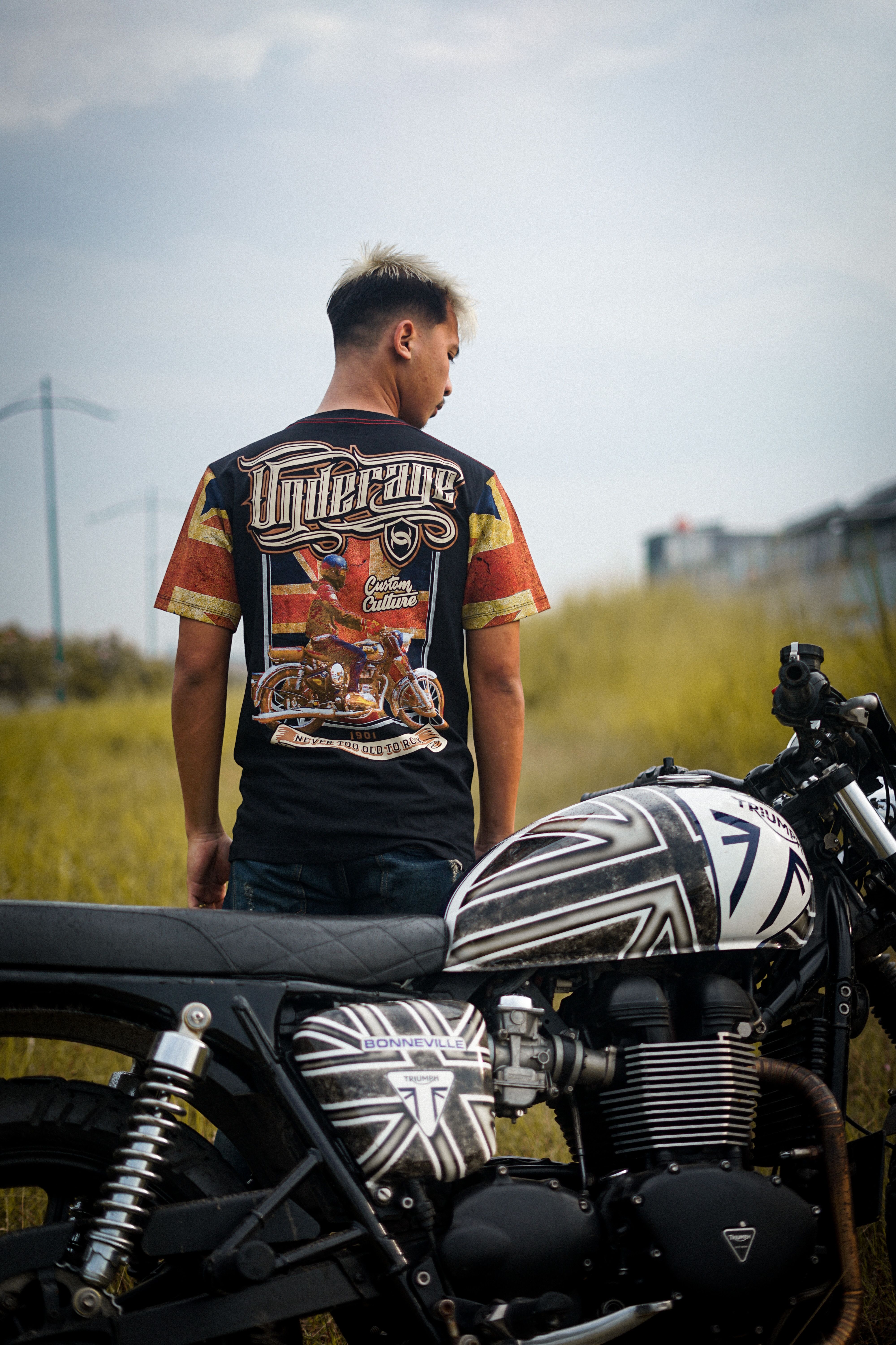 A man stands with his custom motorcycle outdoors, showcasing unique design and style.