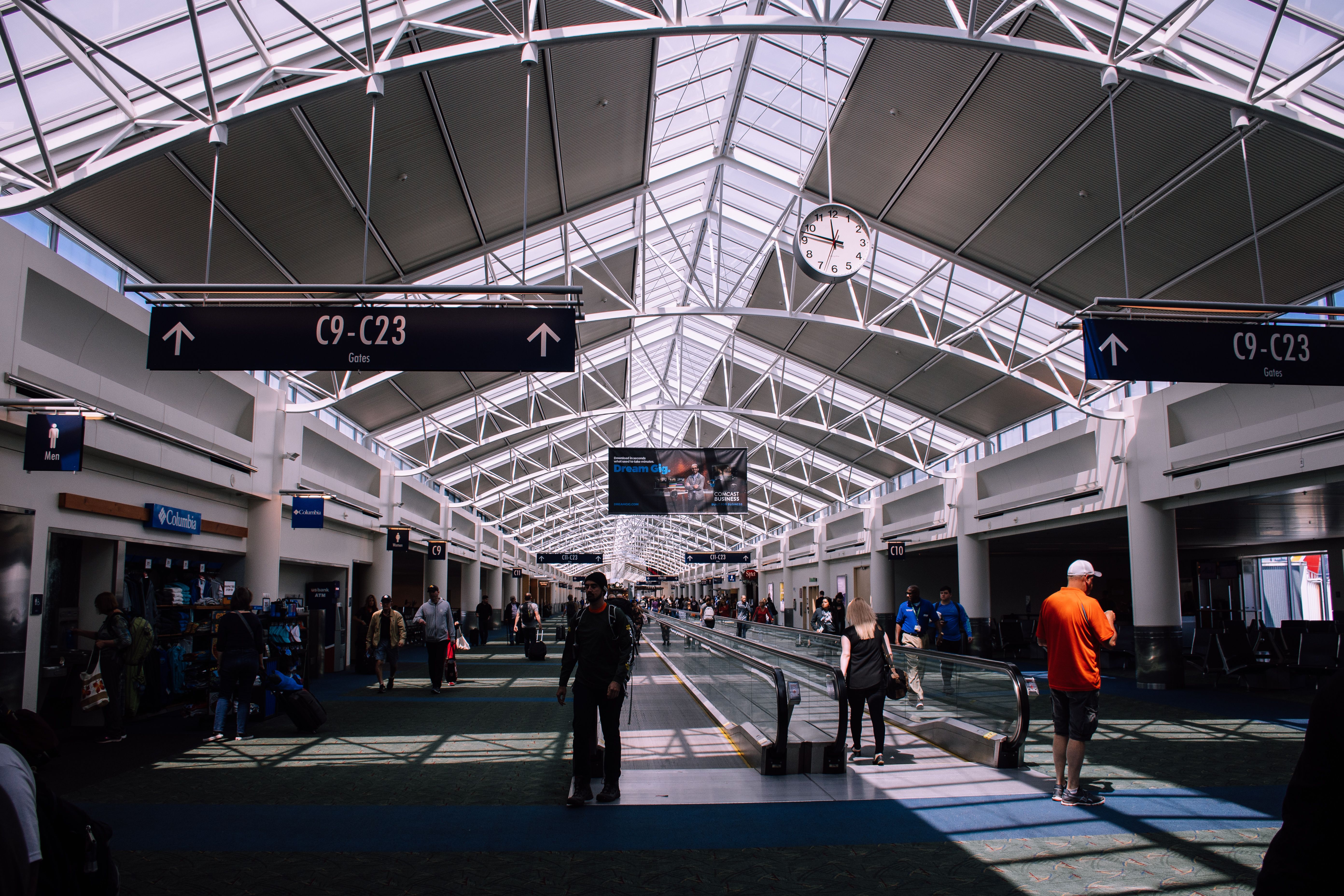 Passengers walk through an airport concourse beneath signs for gates C9–C23