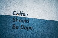 Street art featuring bold statement 'Coffee Should Be Dope' on a concrete wall.
