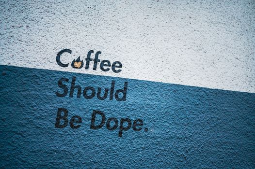Street art featuring bold statement 'Coffee Should Be Dope' on a concrete wall.