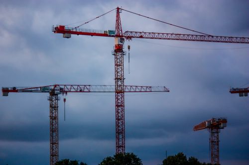 Free Tower cranes stand tall under a dramatic cloudy sky, representing modern industry. Stock Photo
