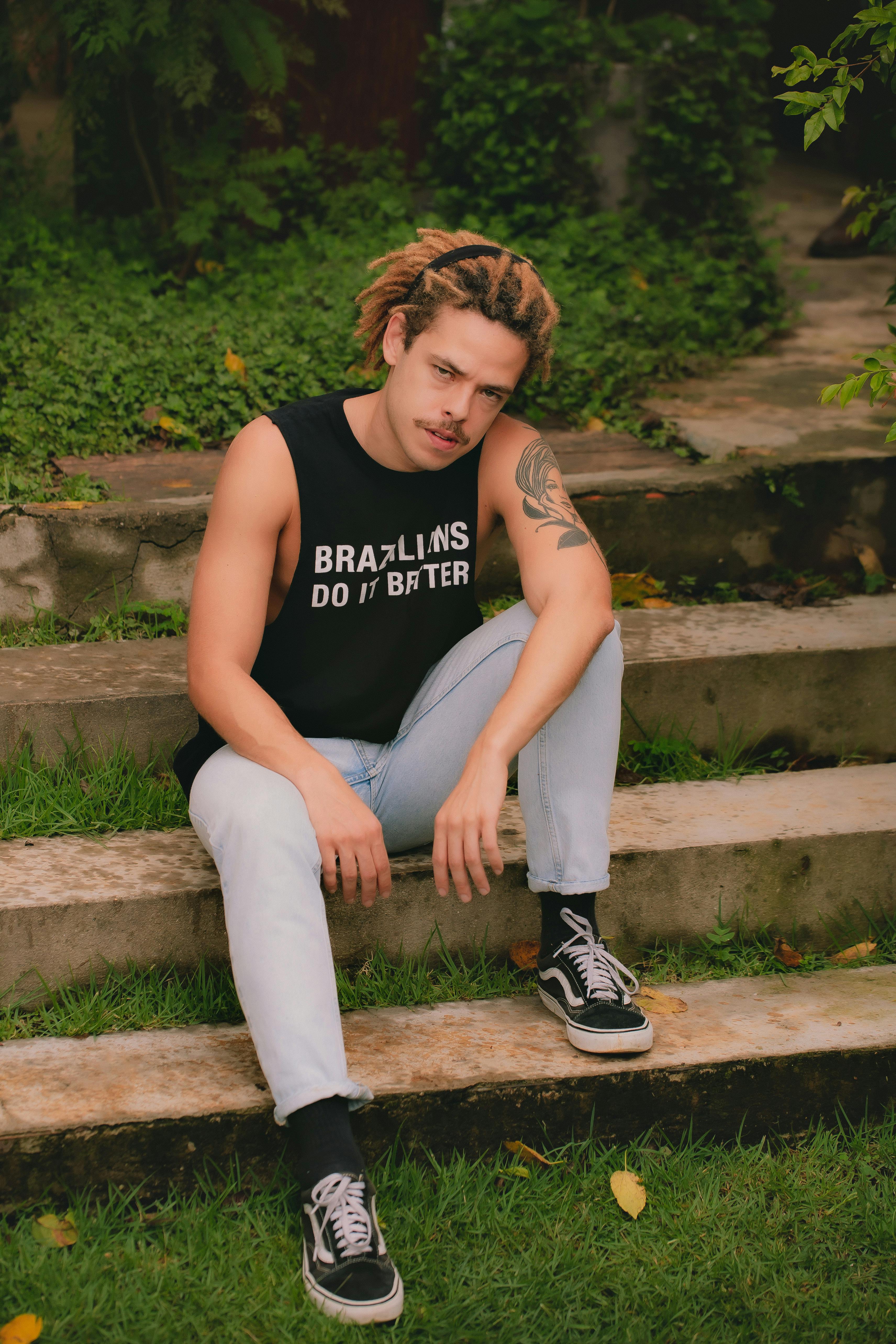 Young man with dreadlocks and tattoos showcasing streetwear fashion sitting on steps.