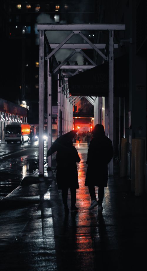 Free Two people walk on a rainy city street at night under an umbrella. Urban silhouettes. Stock Photo