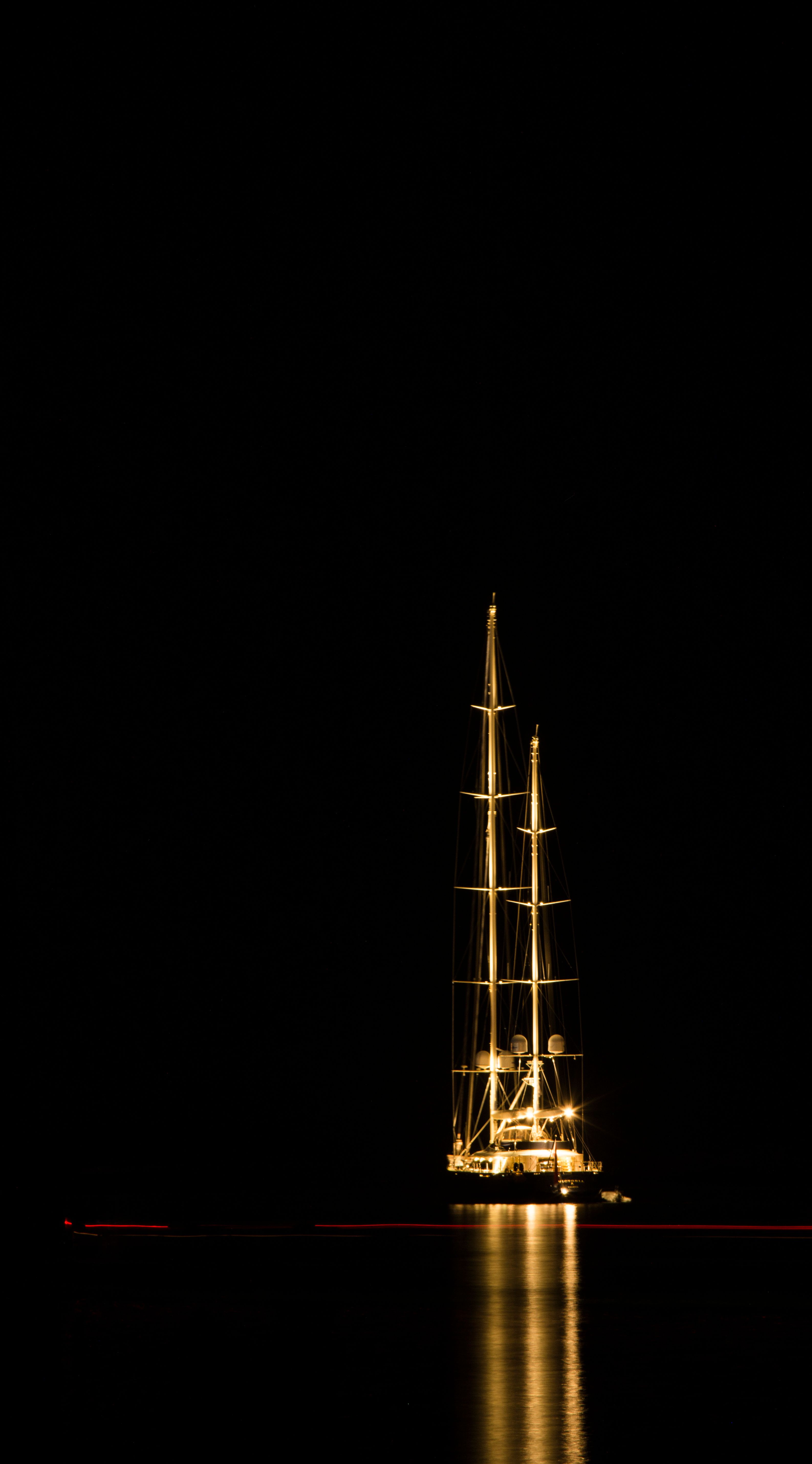 A glowing sailboat at night with reflections on the sea creates a tranquil scene, ideal for nautical themes.