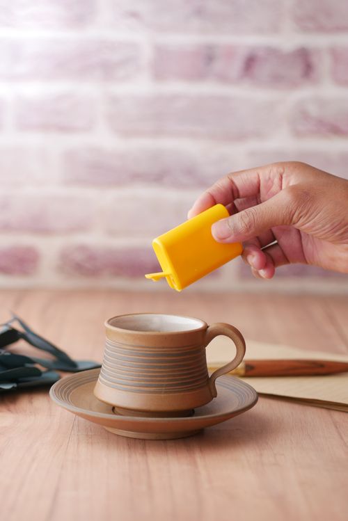 Free A hand pours sweetener into a rustic coffee cup on a wooden table indoors. Stock Photo