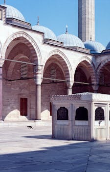 Elegant arches and domes of Süleymaniye Mosque courtyard under clear blue sky in Istanbul.