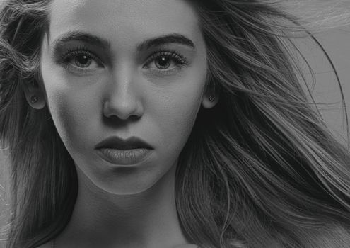 Close-up black and white portrait of a young woman with intense gaze and flowing hair.