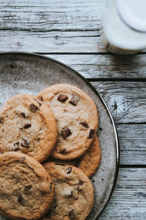 Free Delicious homemade chocolate chip cookies arranged on a rustic wooden table with a glass of milk. Stock Photo