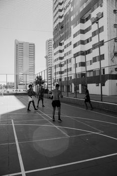 Black and white photo of adults playing basketball outdoors amidst urban surroundings.