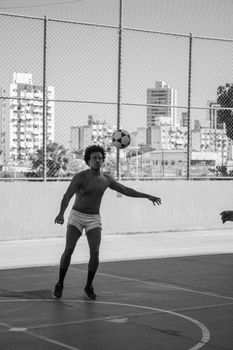 Shirtless man playing soccer in an urban outdoor court. Captured in striking black and white.