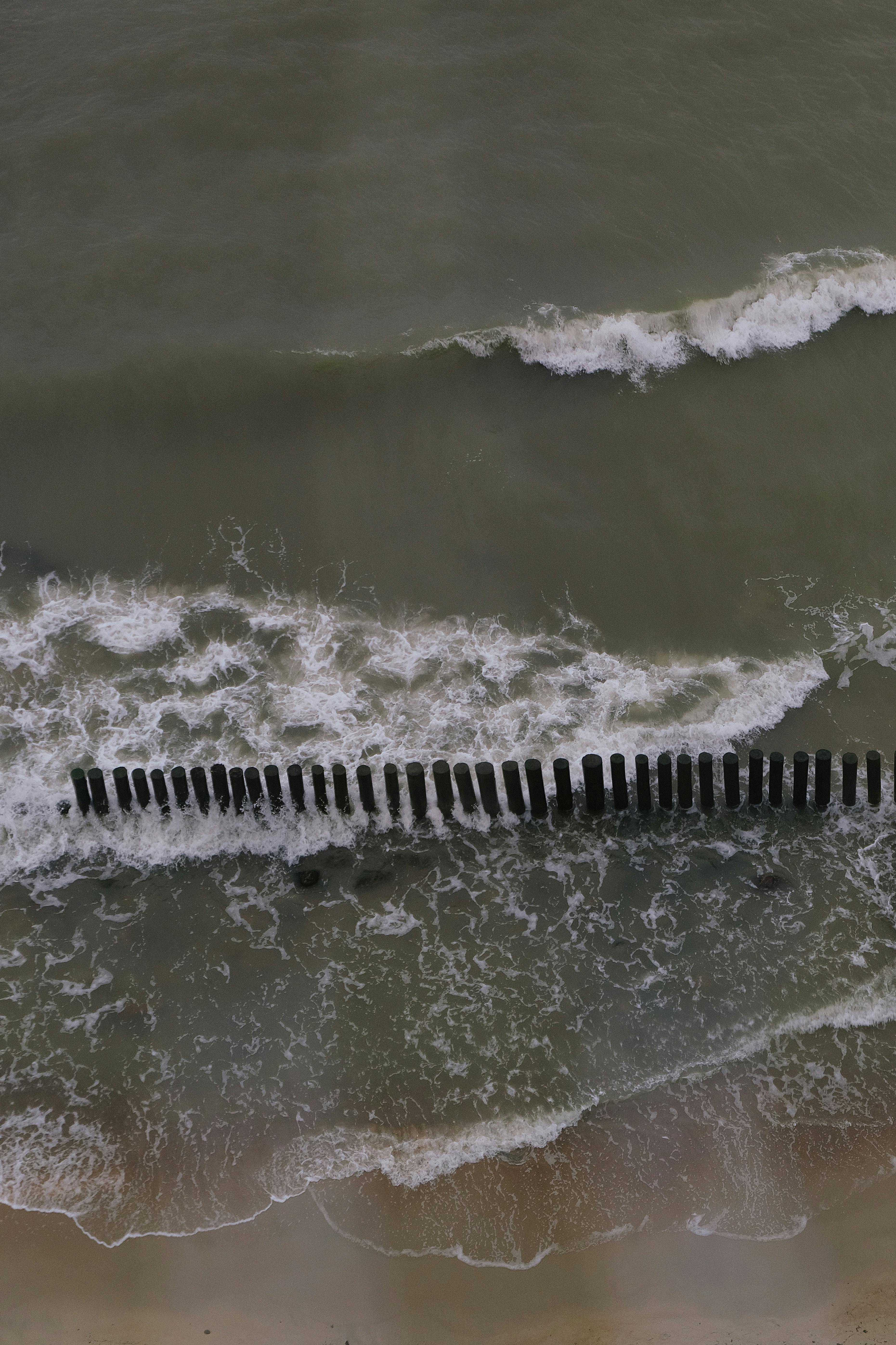 Aerial image of waves crashing against a wooden breakwater on the seashore.