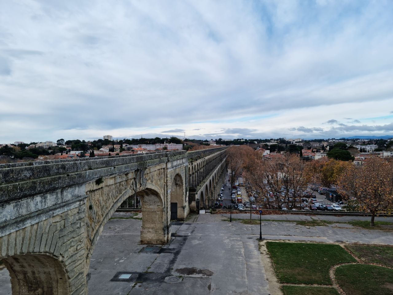 A scenic view of the historic Aqueduc Saint-Clément in Montpellier, showcasing its arches under a cloudy sky.