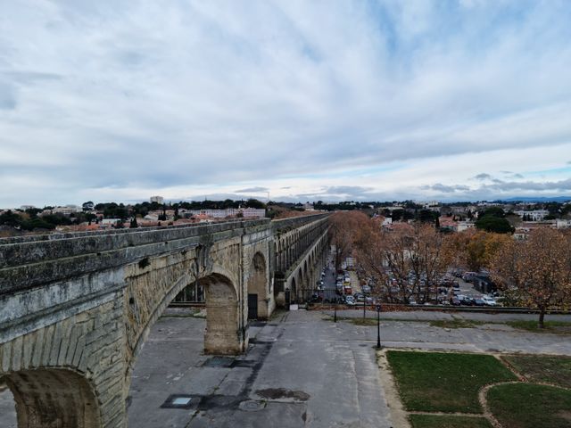 A scenic view of the historic Aqueduc Saint-Clément in Montpellier, showcasing its arches under a cloudy sky.