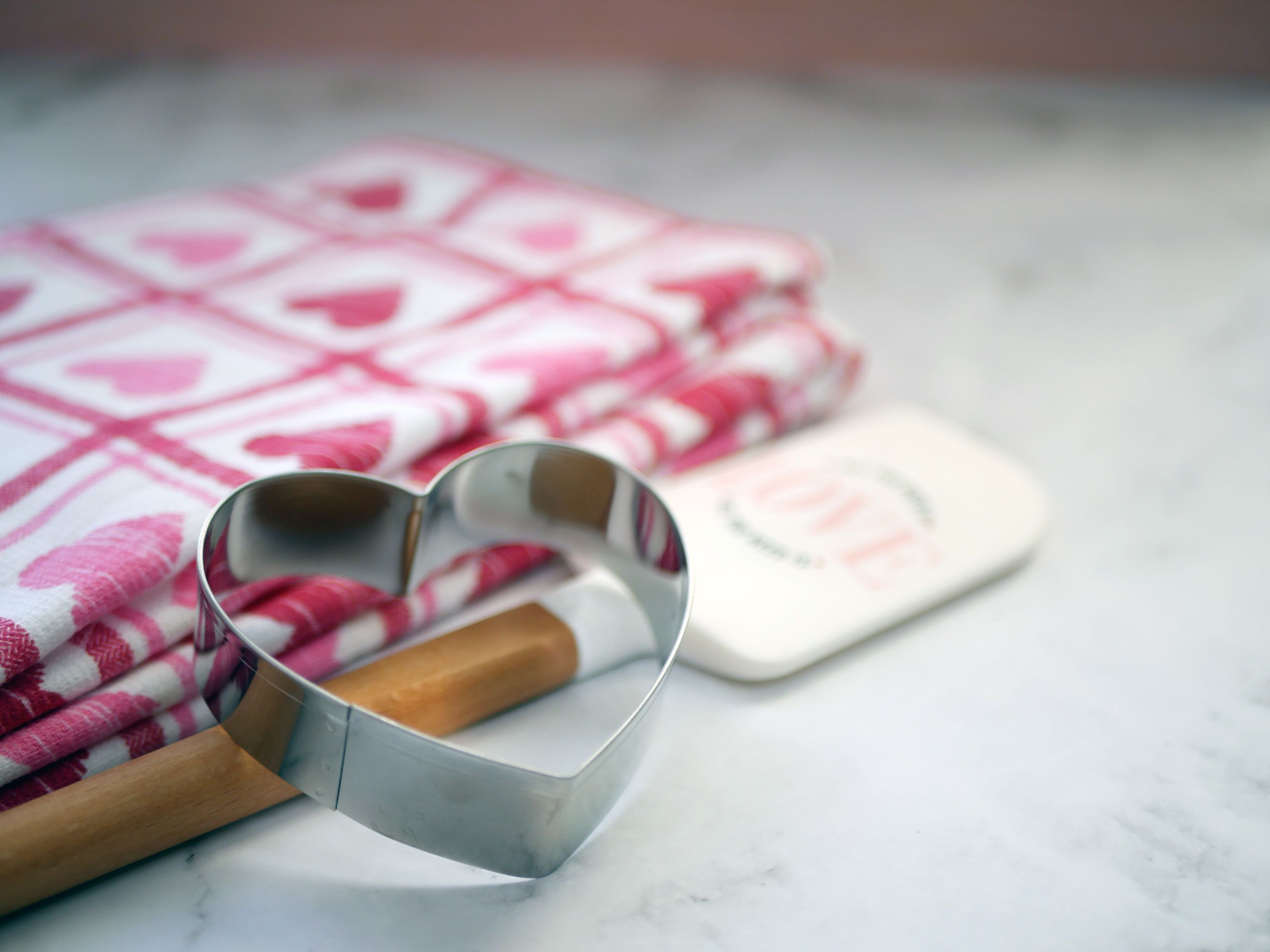 Heart-shaped cookie cutter on marble with pink heart-patterned cloth, perfect for baking themes.