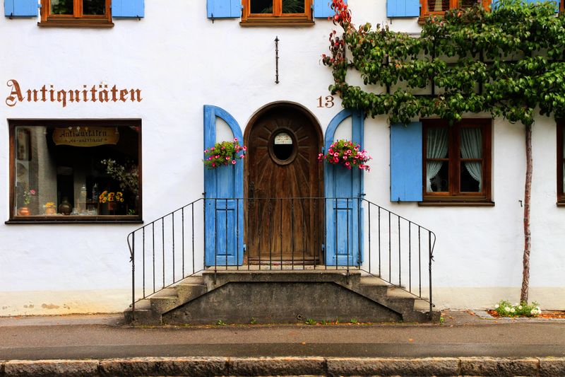 Charming entrance of an antique shop in Oberammergau with rustic wooden door and vibrant shutters.