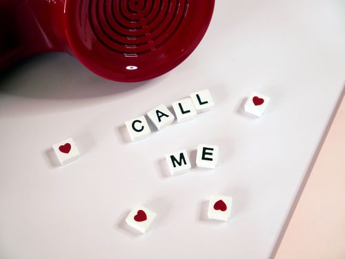 Free Close-up of Scrabble tiles spelling 'Call Me' with a red phone on a textured background. Stock Photo