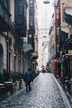 A rainy day in Istanbul with people walking towards the historic Galata Tower on a cobblestone street.