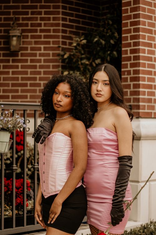 Free Two women pose confidently in chic pink evening dresses against a stylish urban backdrop. Stock Photo