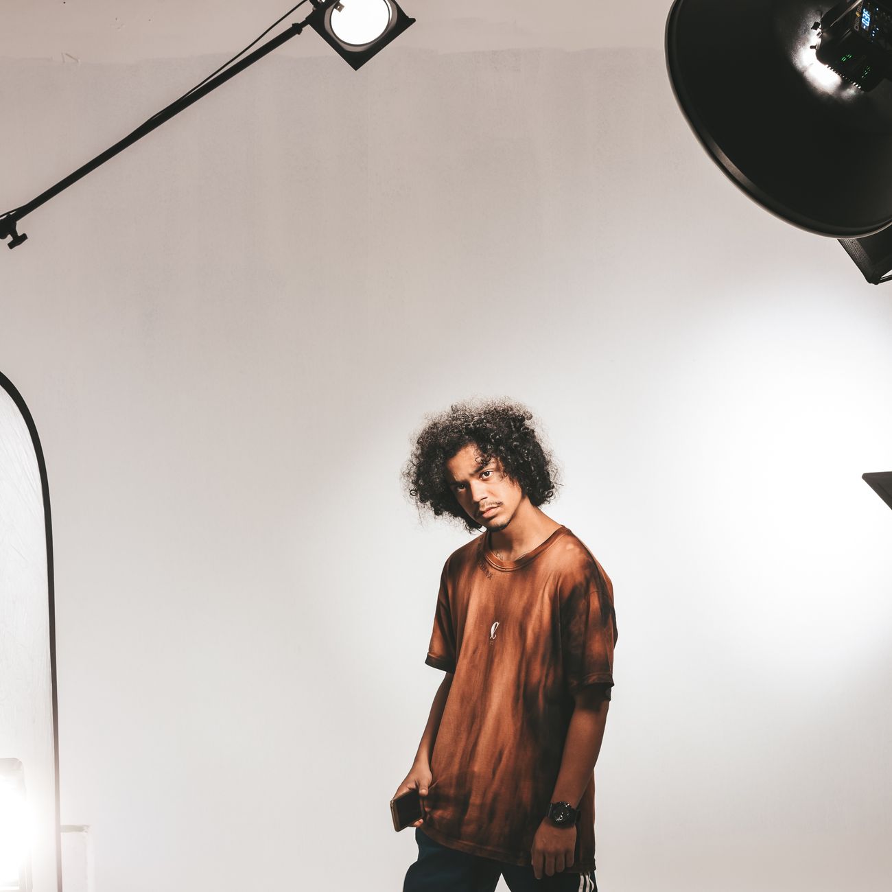 Studio portrait of a young man with curly hair standing under professional light