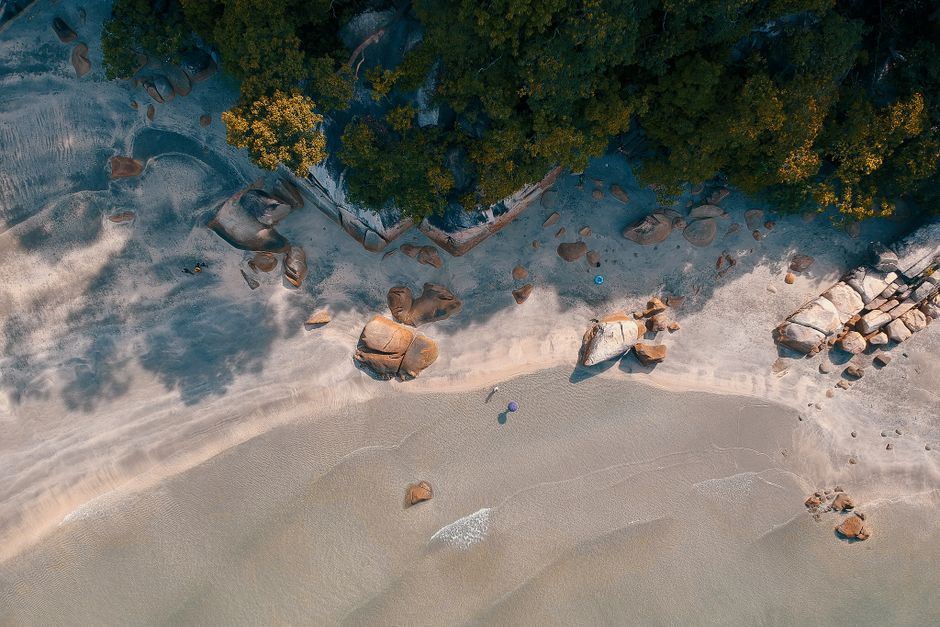 Aerial view of a scenic beach with rocky shorelines and lush foliage.