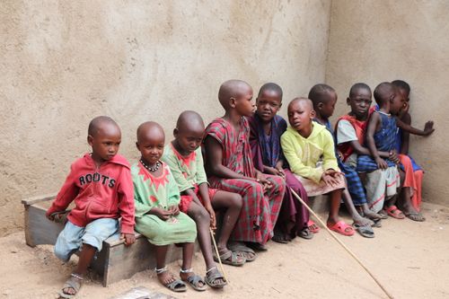 Free Children in colorful clothing sitting together on a wooden bench outside a concrete wall. Stock Photo