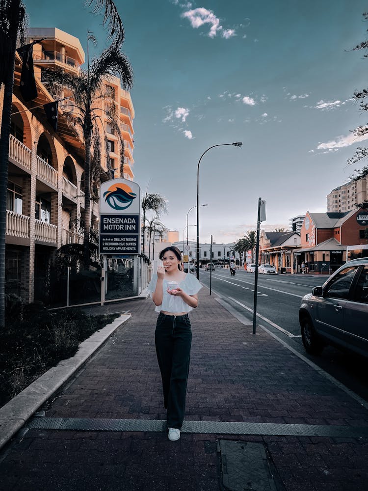 A Woman Walking On The Sidewalk Eating Ice Cream