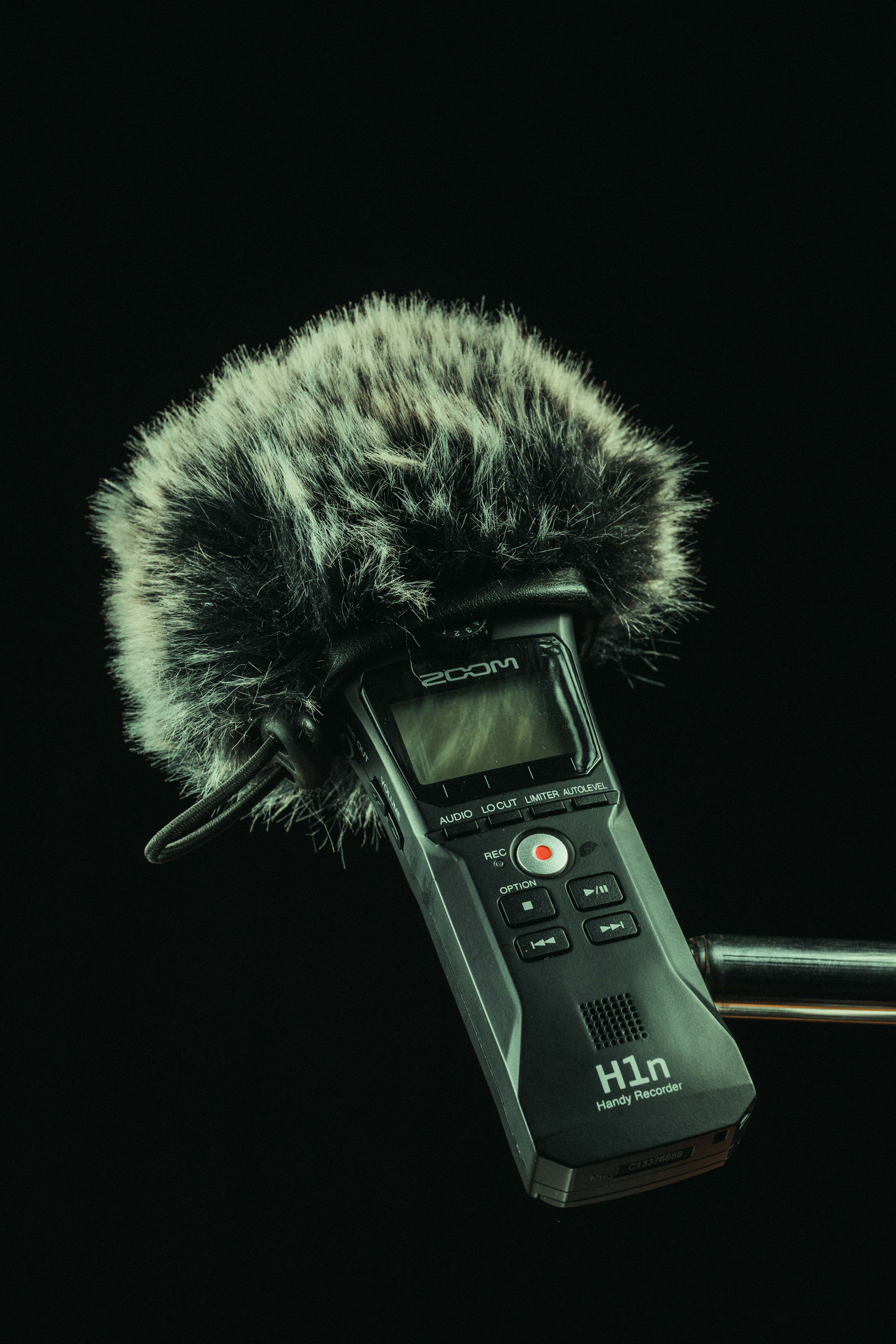 Close-up of a professional audio recorder with a furry windshield against a black background.
