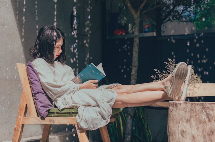 Woman Sitting On Chair While Reading Book