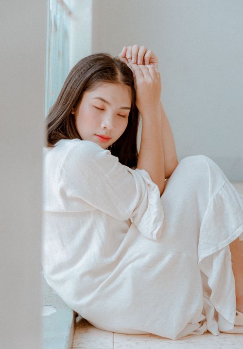 Free Young woman in white dress sitting by a window, embracing serenity. Stock Photo