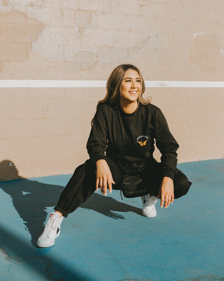 Woman In Black Long Sleeve Shirt And Pants Squatting On Concrete Pavement