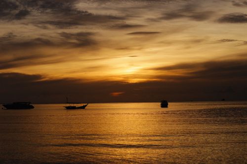 Free Peaceful ocean scene at sunset with boats silhouetted against a golden sky. Stock Photo