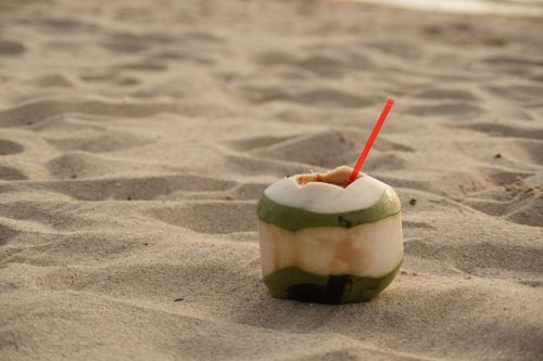 Free Peeled coconut with a straw on a sandy tropical beach, symbolizing summer refreshment. Stock Photo