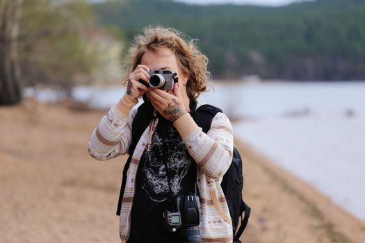 A woman with camera photography capturing nature by a lake on a breezy day.