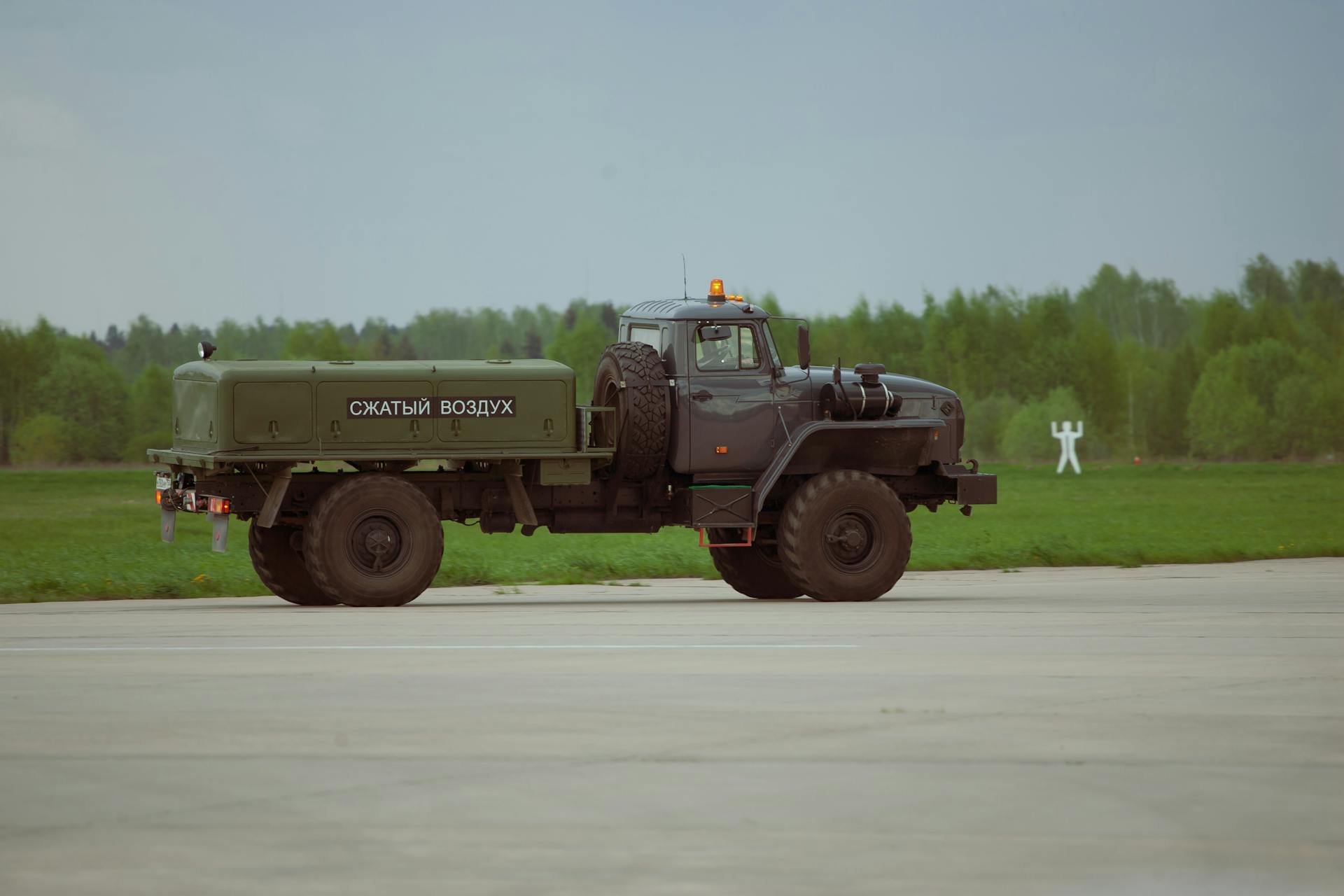 Military truck with compressed air equipment parked on an airfield with green fields in the background.