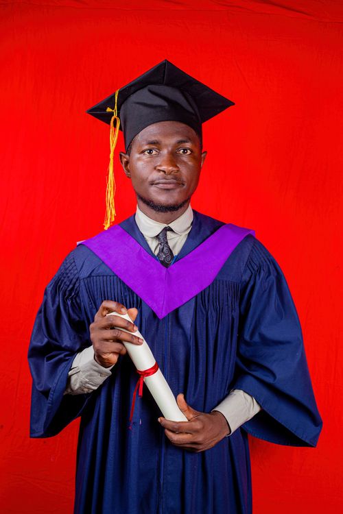 Free Young graduate in cap and gown holds diploma against a vibrant red background. Stock Photo