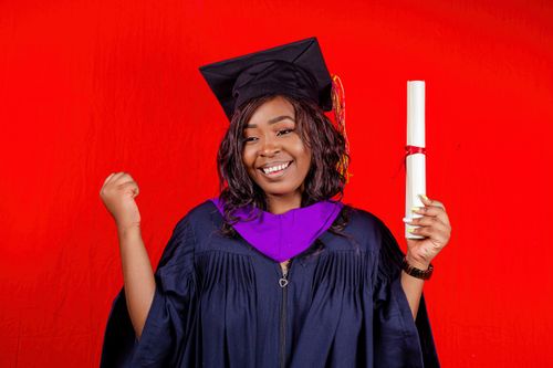 Free Happy young graduate celebrating with diploma against a red background. Stock Photo