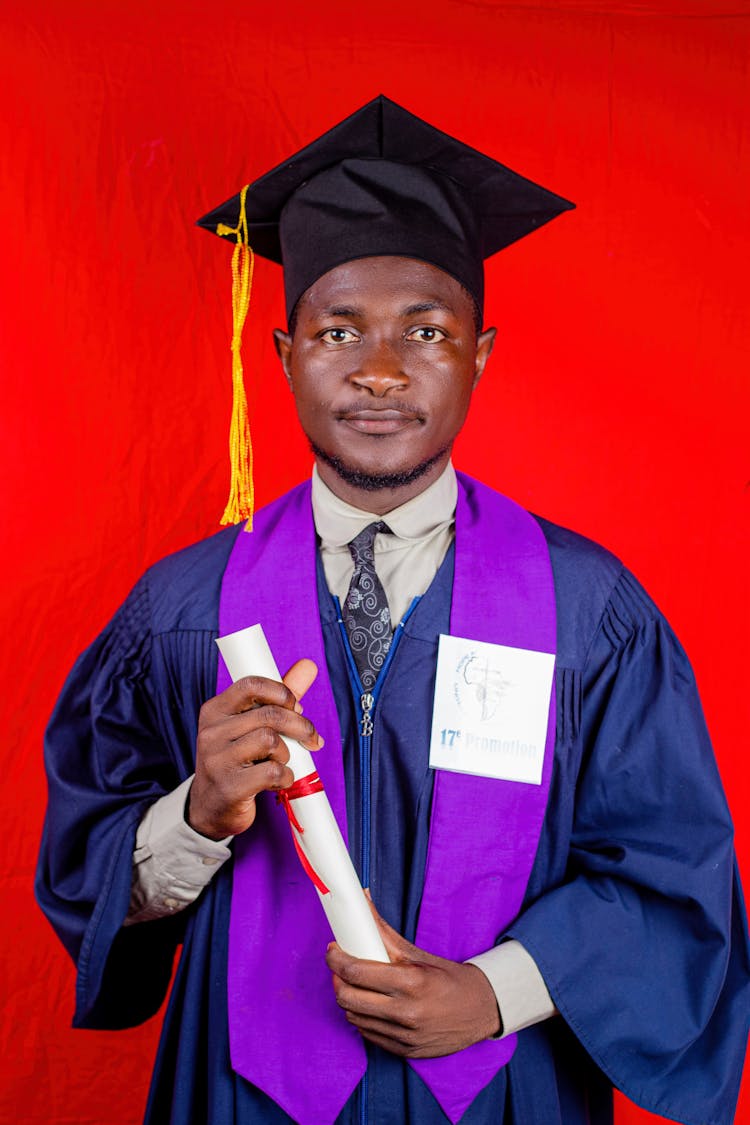 Close-Up Shot Of A Man Wearing Graduation Gown And Square Academic Cap On Red Background