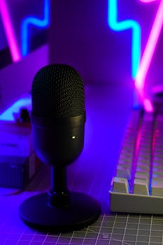 Close-up of a condenser microphone and keyboard in a neon-lit modern workspace. Perfect for creative studios.