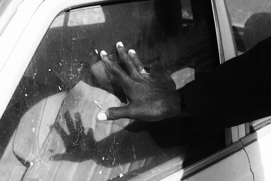 Black and white close-up of a hand placed on a car window, reflecting the subtle contrast and textures in Abuja, Nigeria.